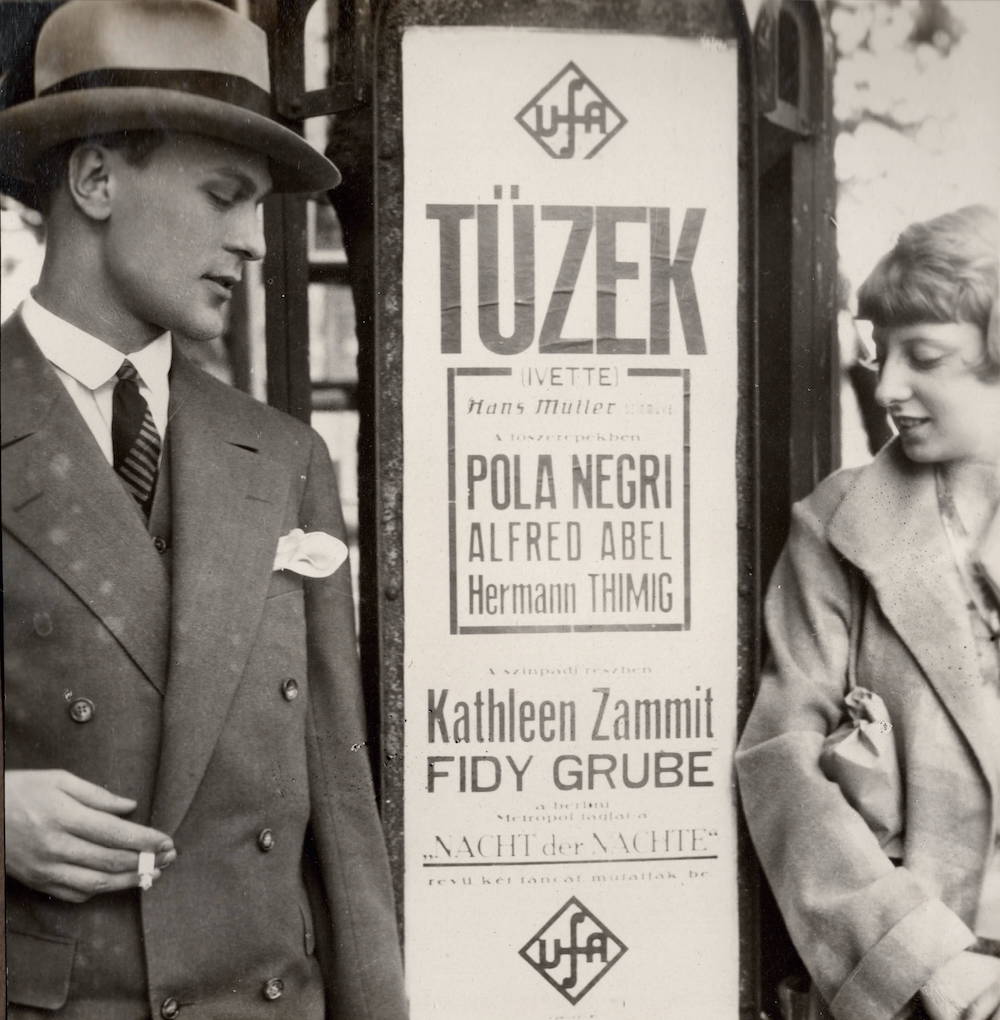 A photo of Fidi Grube and Kathleen Zammit in Budapest against a poster advertising their appearance in Nacht der Nachte from the Berlin Metropol (1927)